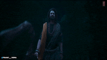 a man with a beard and a necklace of beads is standing in a dark room