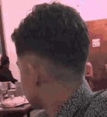 a man with curly hair and a shaved head is sitting at a table in a restaurant .