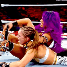 a woman with purple hair is wrestling another woman with blonde hair