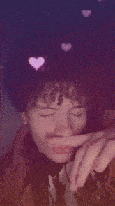 a person with curly hair is covering their nose with their finger while pink hearts are floating around them