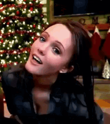 a woman is standing in front of a christmas tree and smiling .