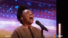 a woman singing into a microphone with a nbc logo in the corner