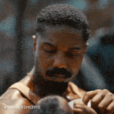 a man with a beard is holding a baby with the hashtag #sinnersmovie below him