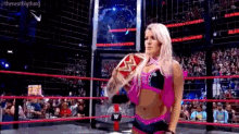 a woman is standing in a wrestling ring holding a wrestling championship belt .