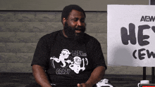 a man sitting in front of a sign that says " he 's crew "
