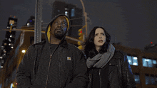 a man in a carhartt jacket stands next to a woman and a man in a daredevil mask
