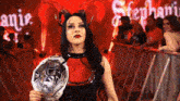 a woman in a devil costume is holding a championship belt in front of a crowd .