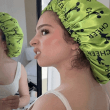 a woman wearing a green cheer bonnet looks at herself in the mirror