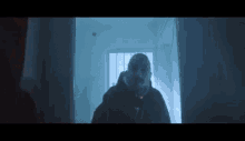 a man in a hooded jacket is standing in a dark hallway in front of a window .