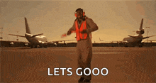 a man in a helmet and safety vest is standing on an airport runway .