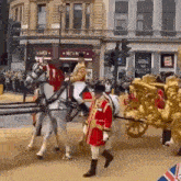 a man in a red and gold uniform is riding a horse drawn carriage down a street .