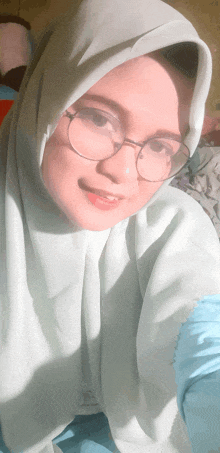 a woman wearing a hijab and glasses is smiling for the camera
