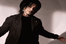 a man wearing a black hat and a black jacket is standing in front of a white wall