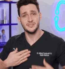 a man wearing a black shirt that says dr. mitchell yardiardi d.o. family medicine holds his hands to his chest