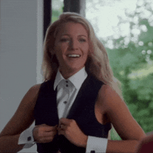 a woman wearing a tuxedo vest and a white shirt smiles