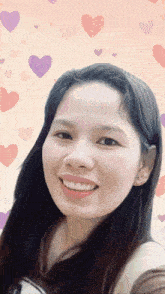 a woman is smiling in front of a pink background with hearts