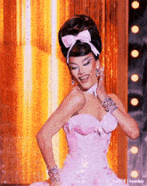 a woman in a pink dress with a bow on her head is standing on a stage .