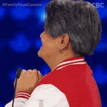 a woman wearing a red and white jacket stands in front of a microphone with the hashtag familyfeud canada