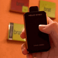 a person is holding a black device that says hello synix