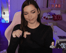a woman in a black shirt is sitting in front of a couch with a xoxo pillow in the background
