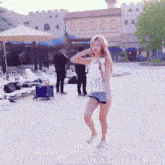 a woman in a white tank top and blue shorts is standing in front of a castle