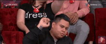 a man wearing a black shirt that says dress is sitting in a chair
