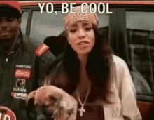 a woman wearing a bandana and a necklace is standing in front of a car and holding a dog .