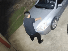 a man is standing next to a silver car in a driveway