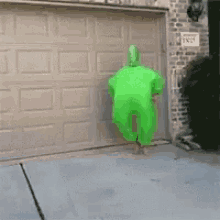 a person in a green costume is jumping in the air in front of a garage .