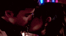 a man and a woman are kissing in front of a neon background