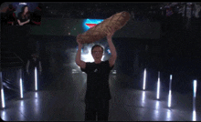 a man in a black shirt is holding a large bread roll over his head