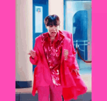 a man in a pink suit and jacket is standing in front of a building .