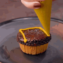 a person is piping yellow frosting on a chocolate cupcake