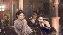 a woman singing into a microphone next to another woman with the ta pro logo on the bottom right