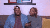 a man and a woman are sitting on a couch looking at their phones