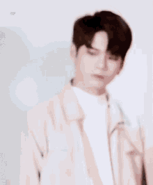 a young man wearing a white jacket and a white turtleneck is looking down .