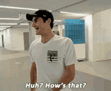 a man in a white shirt is standing in a hallway and asking how 's that .