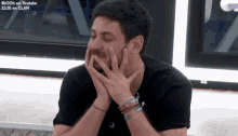 a man is covering his mouth with his hands while wearing bracelets and a black shirt