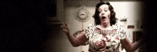 a woman in a floral dress is standing in a dark room with her arms outstretched and a clock in the background .