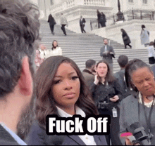 a woman in a suit stands in front of a crowd and says fuck off