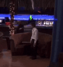 a man in a white shirt is standing in front of a couch and a bar with a sims logo on it