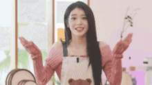 a woman wearing an apron with a teddy bear on it is standing in a room with her arms outstretched .