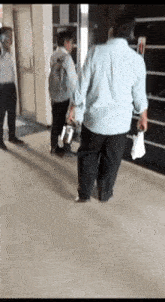 a man in a blue shirt is walking down a hallway with a backpack .