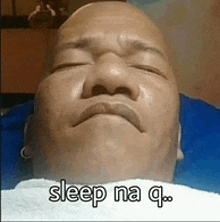 a bald man is laying on a bed with his eyes closed and a towel around his neck .