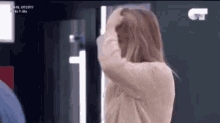a woman covering her face with her hand while standing in front of a tv screen with the number 5 on it