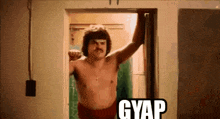 a shirtless man with a mustache is standing in a doorway with the word gyap on it .