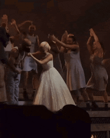 a woman in a white dress is surrounded by a group of people