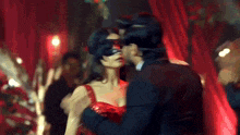 a man and a woman are kissing in a room with red curtains . the woman is wearing a red dress .