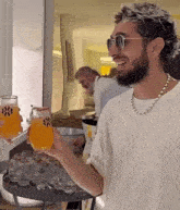 a man wearing sunglasses and a necklace holds up a glass of orange juice
