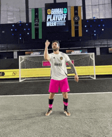 a man in a bimbo jersey stands on a soccer field in front of a sign that says global playoff week